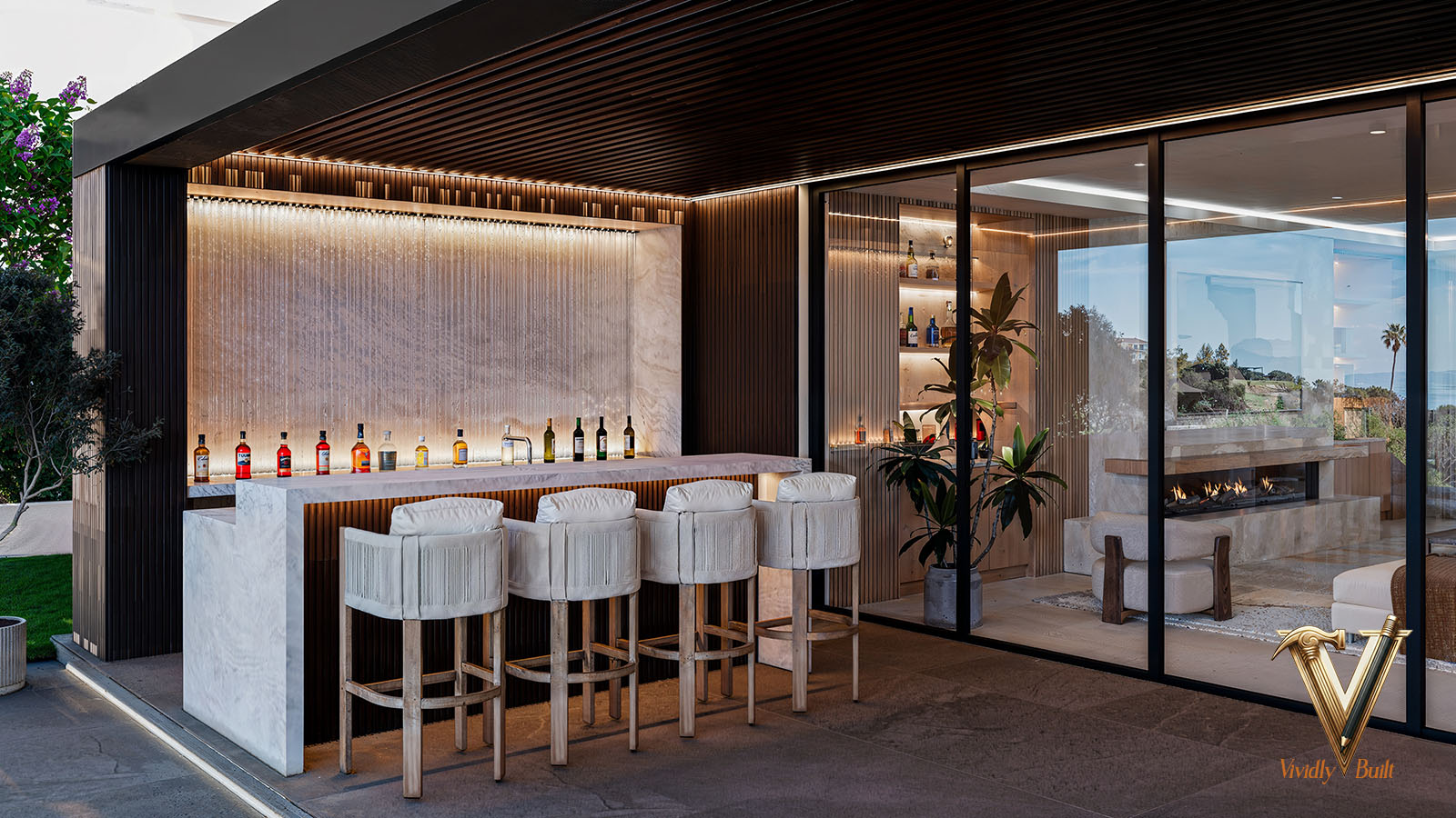 Covered outdoor bar with fluted-glass rain backdrop, marble waterfall counter and see-through fireplace beyond — Modern Estate, Palos Verdes