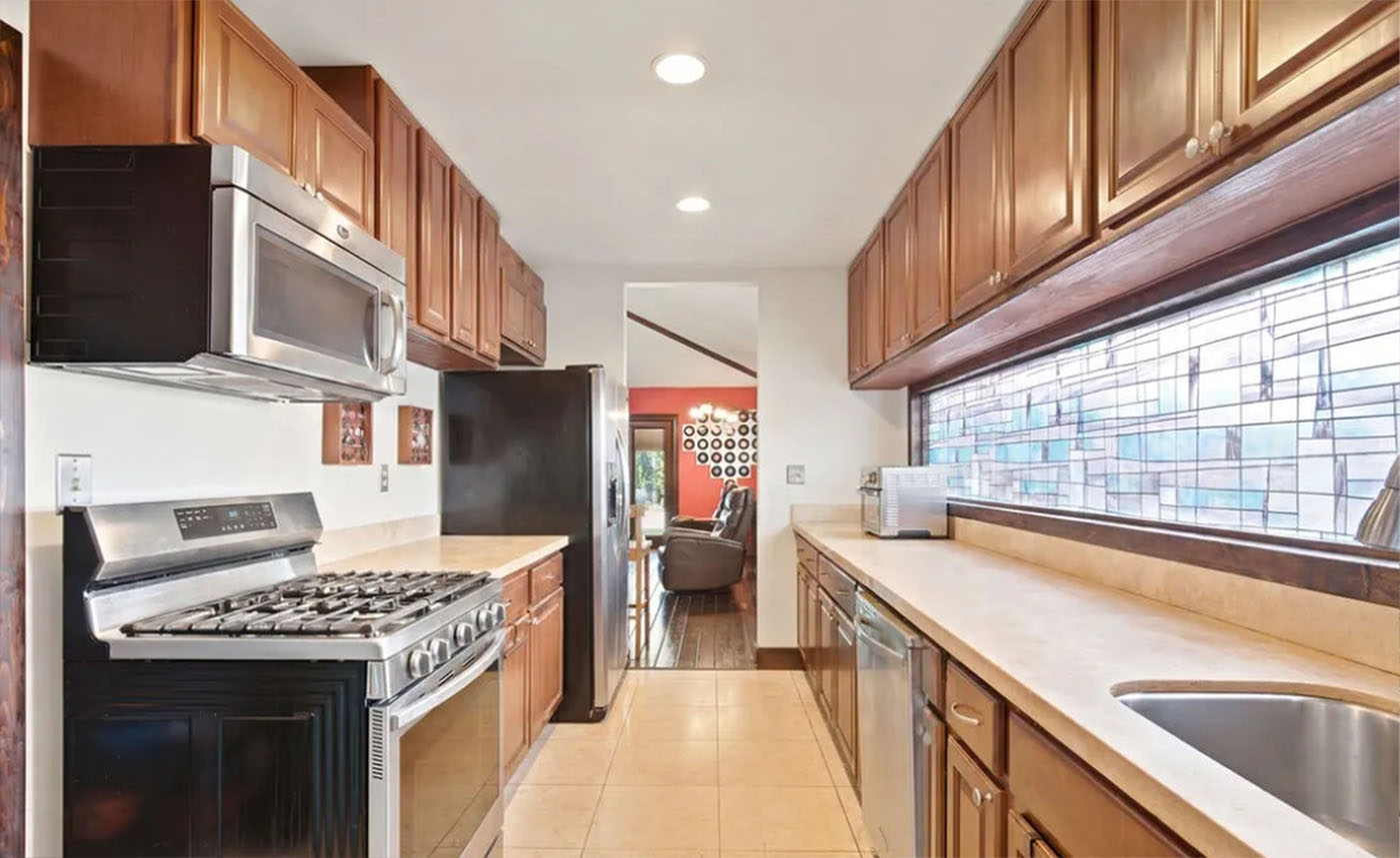 Existing closed galley kitchen with dark wood cabinets and tile floor, walled off from the living room - Santa Monica Spanish bungalow before remodel