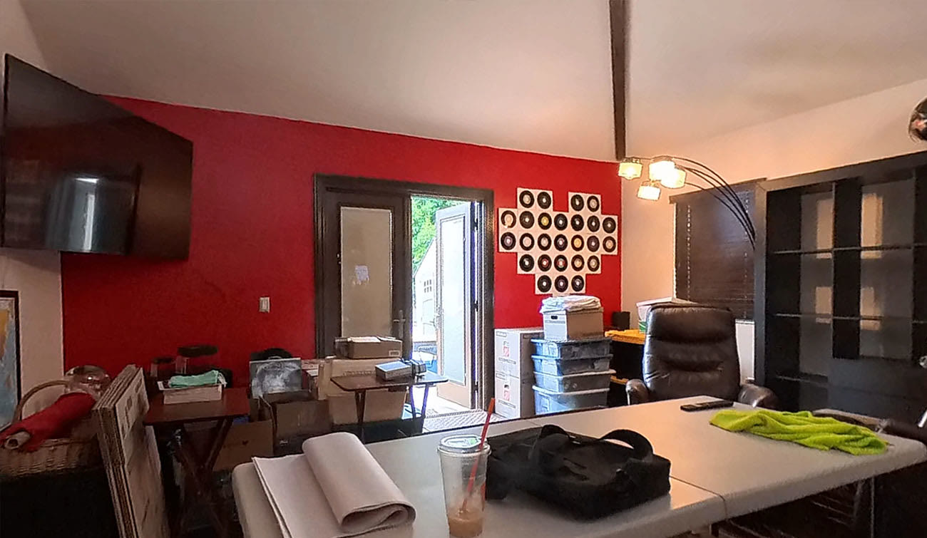 Existing room with a red accent wall, dark French doors and a beamed ceiling, used as a cluttered home office - Santa Monica Spanish bungalow before remodel